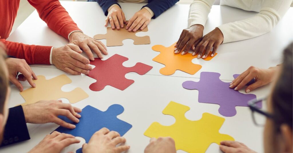 People around a table moving large puzzle pieces together.