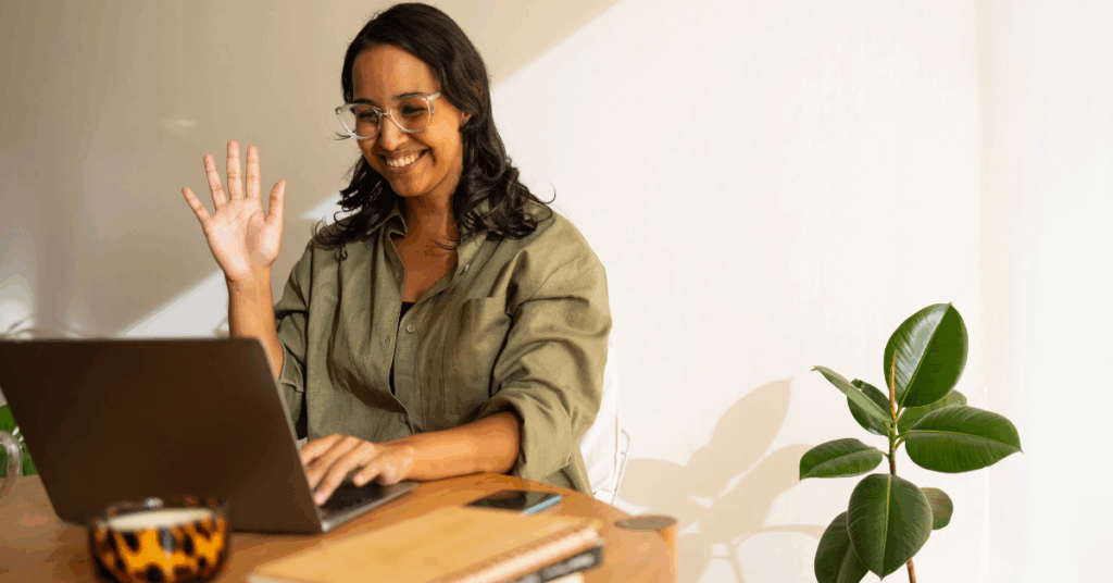 Woman at a desk waving hello in a video call.