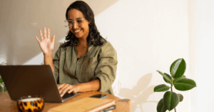 Woman at a desk waving hello in a video call.