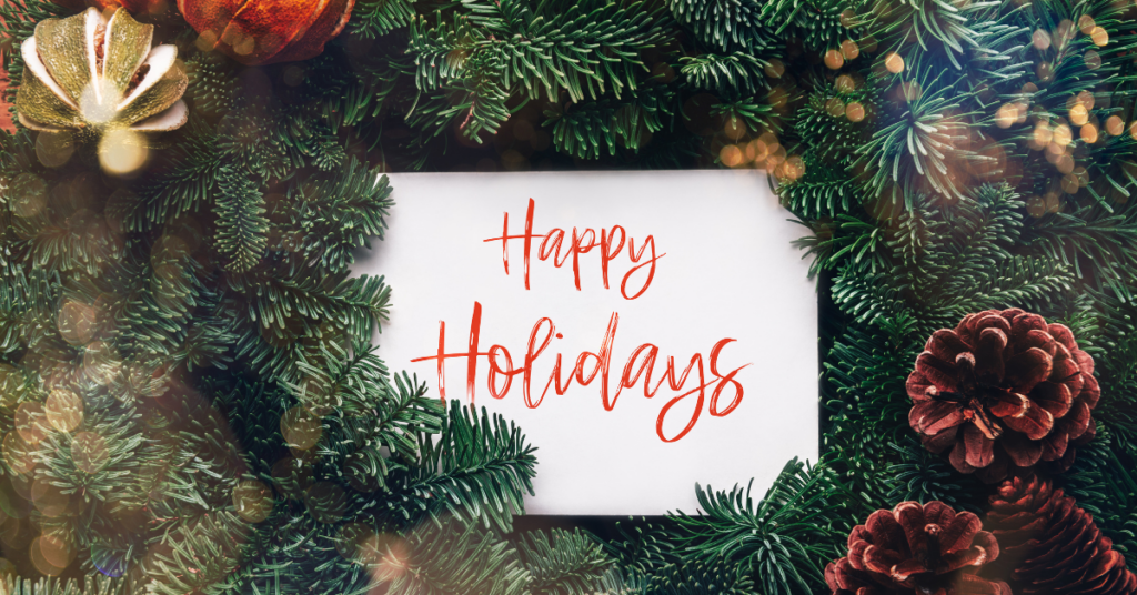 a card in the center of a pine wreath says "happy holidays"