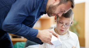 Teacher bending of the desk of a special needs student to help them with their geometry project
