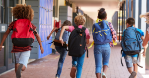 Elementary school students run down a school hallway with backpacks on.